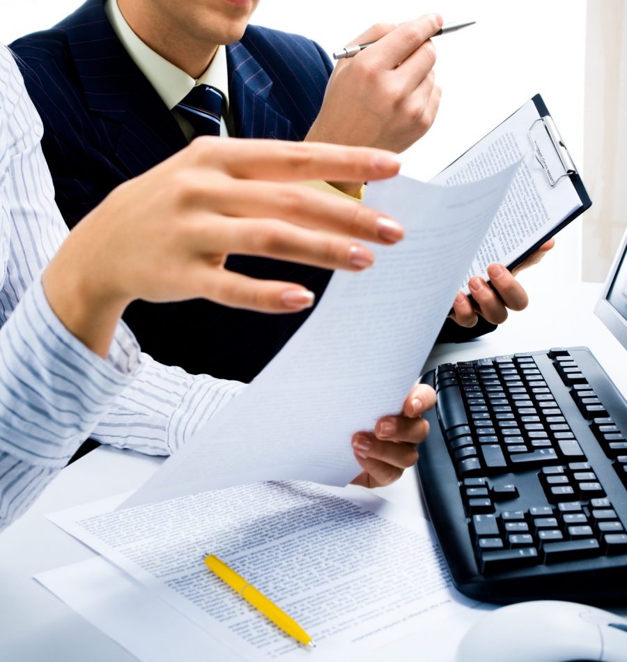 Image of two business partners discussing documents Image of two business partners discussing documents lying on the table with the keyboard and a monitor near by